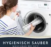A woman is putting a white bath mat into a washing machine. Produktbild-Vorschau
