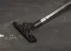 A close-up shot of a vacuum cleaner nozzle on a dark, dusty floor. Náhled obrázku produktu