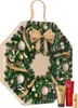 A Christmas advent calendar shaped like a wreath, decorated with pine branches, ornaments, and a large bow. Two tubes of cosmetic products are placed in the foreground. Produktbild-Vorschau