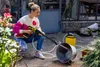 A woman is using a handheld pressure washer in a garden setting. Produktbild-Vorschau