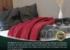 A red blanket draped over a bed with pillows and decorative items. Produktbild-Vorschau