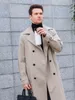A man in a trench coat holding a white thermos, standing in front of a stone wall. Anteprima dell’immagine prodotto