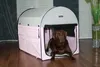 A chocolate labrador dog is lying inside a pink and gray dog crate. Produktbild-Vorschau