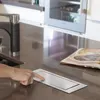 A person's hand is shown pressing a button on a kitchen counter, next to an open book. Anteprima dell’immagine prodotto