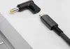 A close-up shot of a USB-C to DC barrel jack adapter and a USB-C cable, placed on a light gray surface next to a silver laptop. Anteprima dell’immagine prodotto