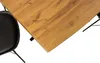 A close-up view of a wooden table with a black chair leg. Produktbild-Vorschau