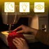A person is using a sewing machine to sew a red fabric. There are icons indicating night mode, a light bulb, and an eye above the sewing machine. Podgląd zdjęcia produktu