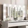 A white vanity table with a large illuminated mirror, reflecting a window with trees outside. Makeup and decorative items are placed on the table. Náhled obrázku produktu