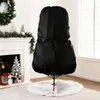 A black Christmas tree storage bag is shown covering a Christmas tree on a white fluffy tree skirt, with a fireplace and decorations in the background. Produktbild-Vorschau