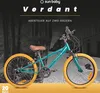 A teal bicycle with yellow tires is shown in a street setting with a blurred background of trees and buildings. Produktbild-Vorschau