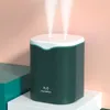 A dark green humidifier with two streams of mist rising from the top, placed on a white pedestal in front of a pink and teal background. Náhled obrázku produktu