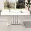 A white extendable dining table with silver legs is shown in a well-lit room with a large window overlooking a garden. Produktbild-Vorschau