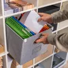 A person is placing papers into a gray fabric storage box with hanging file folders inside, which is placed on a white shelf unit. Anteprima dell’immagine prodotto