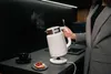A person is holding a white electric kettle in a modern kitchen setting. Voir les images du produit
