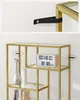 A close-up shot of a modern gold bookshelf with glass shelves, displaying decorative items and books. Náhled obrázku produktu