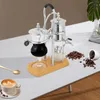 A siphon coffee maker is displayed on a white table with coffee beans and a cup of coffee. Náhled obrázku produktu