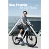A man is riding an electric bicycle in an urban environment with a modern building in the background. Produktbild-Vorschau