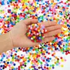 A hand holding a pile of colorful pompons, with many more pompons scattered in the background. Produktbild-Vorschau