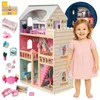 A young child stands next to a multi-story dollhouse, with various dollhouse furniture and accessories arranged around it. A circular inset shows the dollhouse illuminated at night. Voir les images du produit