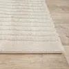A close-up view of a textured rug with horizontal stripes, placed on a wooden floor. Produktbild-Vorschau