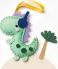 A felt dinosaur craft project with headphones and spots, next to a small felt palm tree. Produktbild-Vorschau