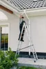 A man is cleaning a gutter while standing on a ladder outside a house. Produktbild-Vorschau