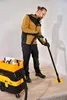 A man is using a sander connected to a vacuum cleaner on a floor near a wall. Podgląd zdjęcia produktu