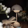A dim table lamp illuminates a book, a cup of coffee, and flowers on a wooden table. Produktbild-Vorschau