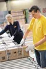 Two people working in a warehouse, handling boxes on a conveyor belt. Produktbild-Vorschau