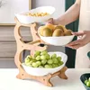 A three-tiered fruit stand made of bamboo, filled with various fruits and snacks, being held by a person. Náhled obrázku produktu