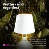 A white lamp with water droplets on it, illuminated from within, set against a dark, leafy background with rain falling. Anteprima dell’immagine prodotto