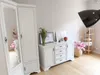 A bright and airy room with a white dresser and wardrobe, decorated with flowers and framed pictures. Náhľad obrázku produktu