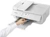 A hand is shown inserting a printed photo into the output tray of a white Canon printer. Podgląd zdjęcia produktu