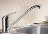 A chrome kitchen faucet is shown over a stainless steel sink, with a textured light beige backsplash in the background. Produktbild-Vorschau
