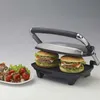 A grill with two burgers on it, and a plate of appetizers to the side. Produktbild-Vorschau