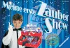 A young boy dressed as a magician is holding a magic wand and standing next to a magic show stage with props. Podgląd zdjęcia produktu