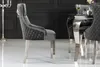 A close-up side view of a gray velvet dining chair with silver legs, placed in a room with a black wall and a reflective floor. Produktbild-Vorschau