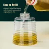 Oil is being poured into a clear, ribbed spray bottle. Text overlays describe the product's refillability. Podgląd zdjęcia produktu