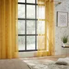 A room with a large window covered by yellow sheer curtains, a brick wall, and a rug on the floor. Podgląd zdjęcia produktu