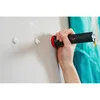 A hand holding a black and red flashlight-like object, pointing it at a light gray wall with two small white blobs on it. Produktbild-Vorschau