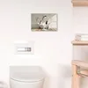A bathroom scene with a toilet, a flush plate, and a canvas print of penguins in a bathtub on the wall. Produktbild-Vorschau