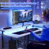 A woman is sitting at a white L-shaped gaming desk with dual monitors, illuminated by blue LED lights. The desk has a headset holder and a lamp. Náhled obrázku produktu
