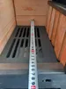 A close-up view of a metal grate inside a fireplace or oven, with a measuring tape placed vertically on top of it. Produktbild-Vorschau