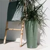 A green planter with a plant is placed next to a bamboo ladder with a green cloth draped over it, against a white wall. Voir les images du produit