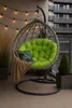 A hanging chair with a green cushion and a tan blanket on a balcony. Voir les images du produit