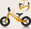 A golden balance bike is shown against a light beige background. An inset circle shows a hand holding the handlebars. Produktbild-Vorschau