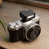 A camera with an attached flash sits on a wooden surface, with a plant in the foreground. Podgląd zdjęcia produktu