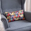 A colorful geometric patterned pillow rests on a gray armchair. Produktbild-Vorschau