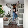A woman is standing on a stepladder and changing a light bulb in a hallway with stairs. Anteprima dell’immagine prodotto