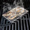 A stainless steel smoker box filled with wood chips sits on a grill grate, with smoke rising from it. Náhled obrázku produktu